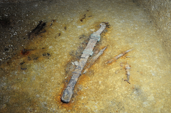 土の穴の中から鞘のついた錆びた刀剣が発掘された時の写真。