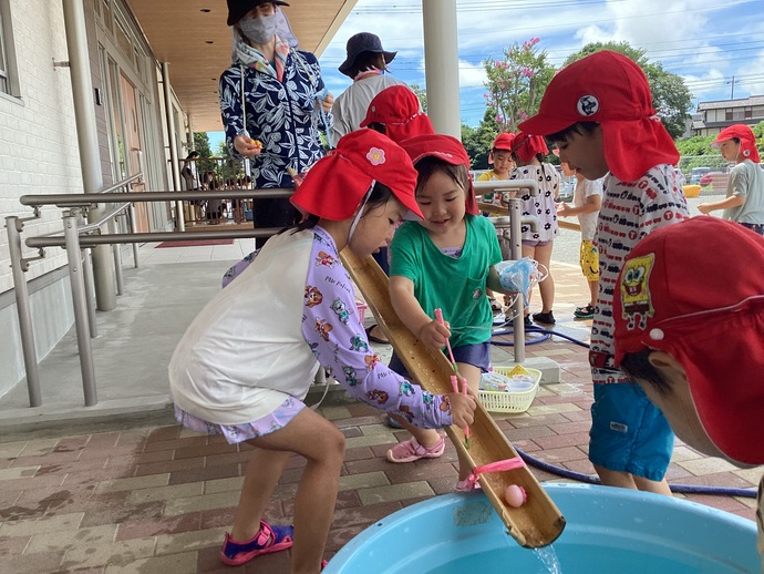 流しそうめんごっこをして遊ぶ子ども達の写真