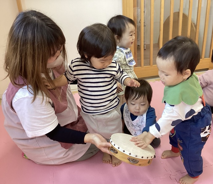 タンバリンに興味を示し、たたいて音を鳴らして楽しむ1歳児の写真。