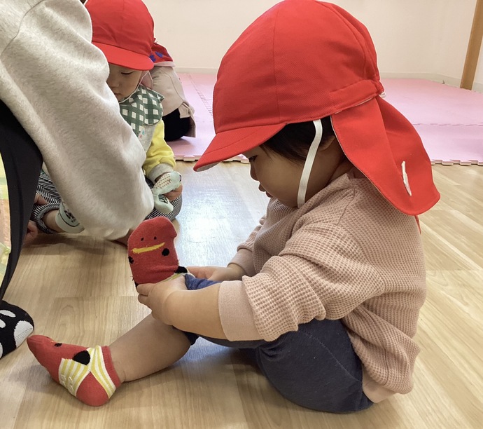 自分で靴下をはこうと頑張って挑戦している0歳児クラスの子どもの写真。