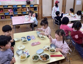 自分の箸やフォークを使って嬉しそうに給食を食べる2歳児の写真