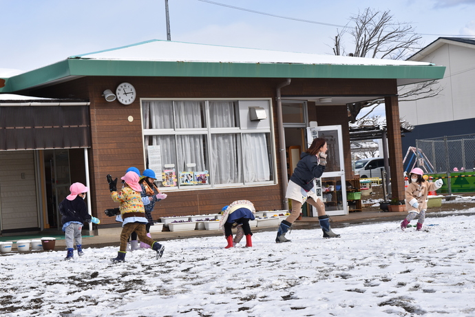 園庭で園児と先生が雪合戦をしている