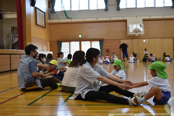 床に座り、足を広げた姿勢で向かい合って手をつなぐ親子