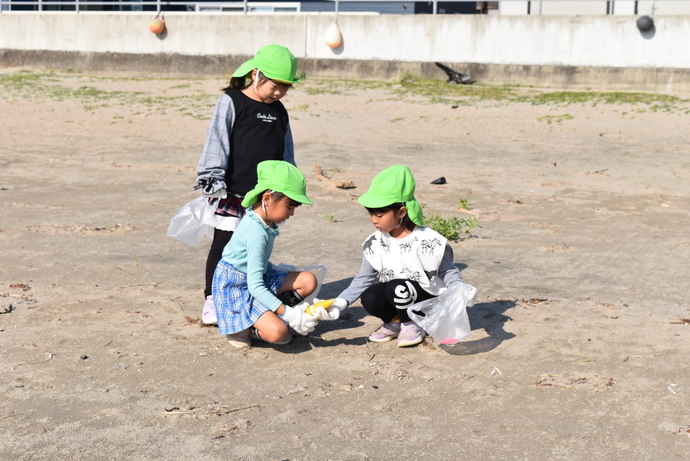 砂浜にしゃがんでゴミを拾う園児