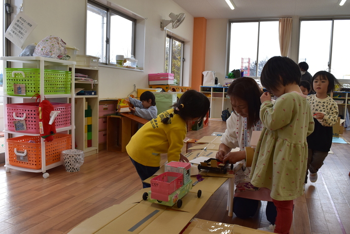 積み木の道路に車を走らせる園児