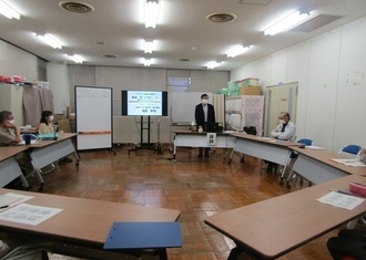 5名の参加者が、円の形に並べた机椅子に座っている写真