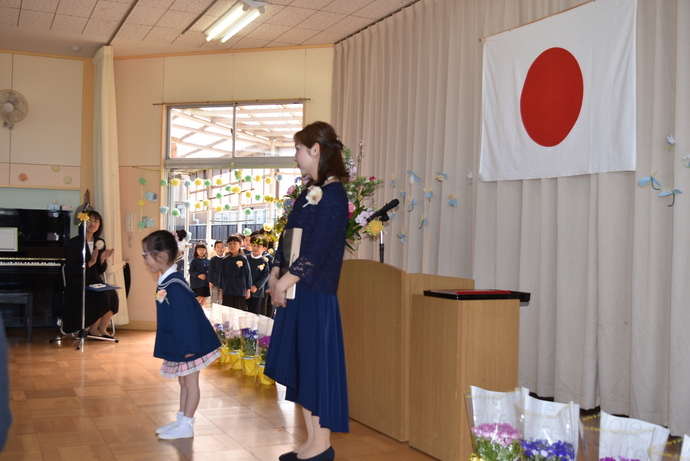 演台の前に立つ先生と、お辞儀をする園児