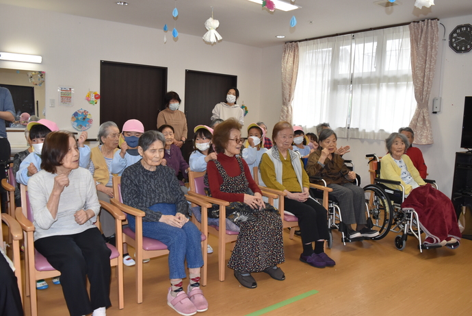 おじいさんおばあさんの座る椅子の後ろで肩たたきをする園児たち